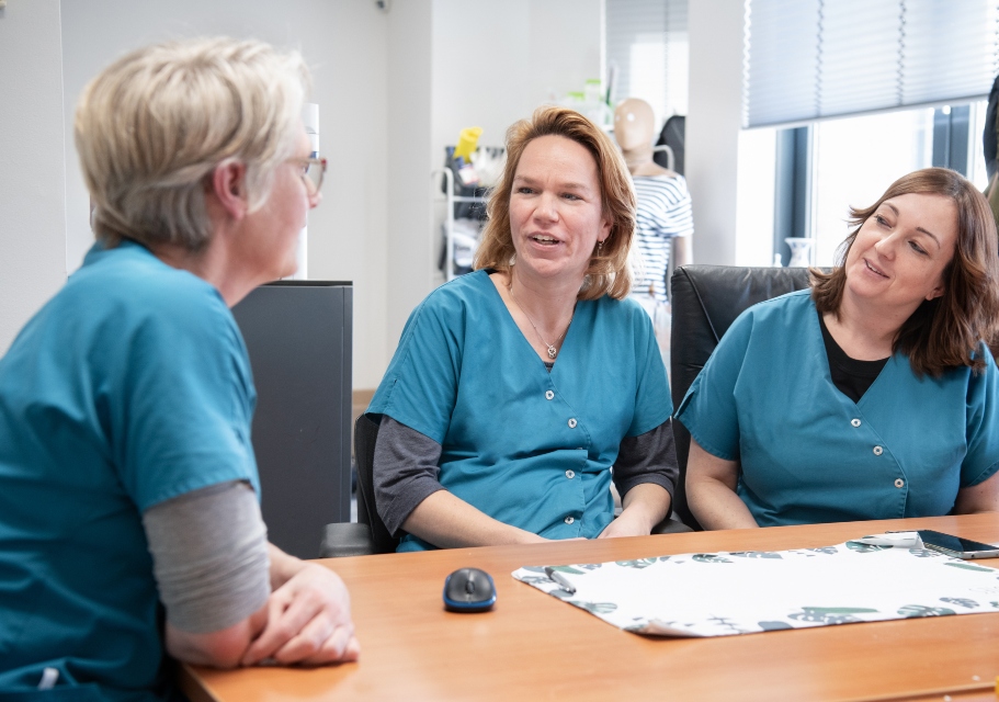 Drie verpleegkundigen in de wijk praten aan een tafel over zeggenschap.