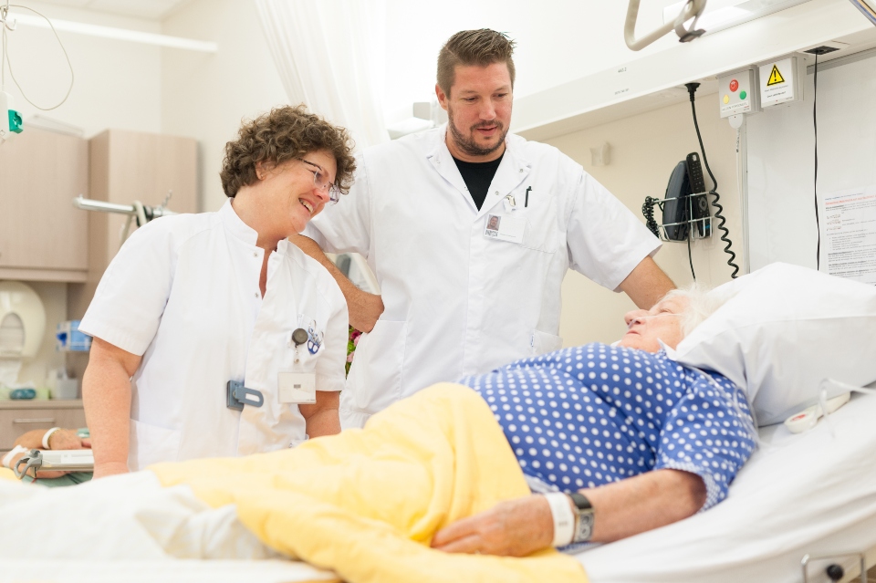 Samen beslissen. Twee verpleegkundigen bij een patiënt in bed.