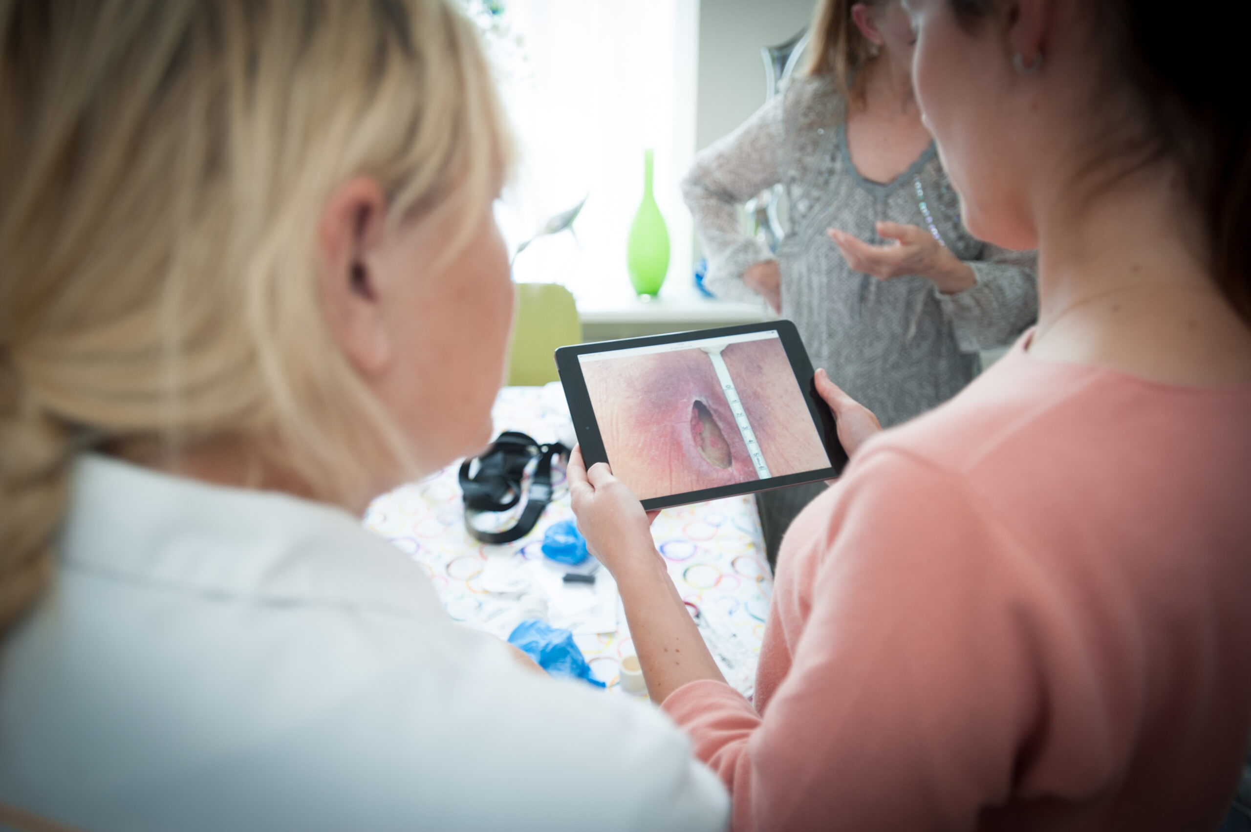 Verpleegkundige en mantelzorger bekijken foto van wond op tablet